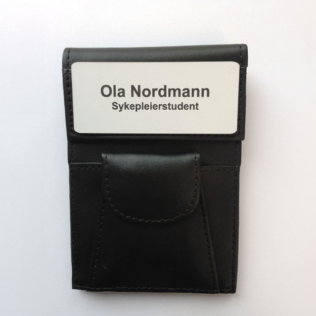 Skinnmappe med navneskilt for sykepleier. Den klassiske skiltmappen brukt av sykepleiere og helsepersonell i mange år. Med skinnlomme for penner, saks osv. Festes i brystlomme på uniform.
