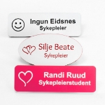 Navneskilt for sykepleier med nål eller magnet. Gravert navneskilt med navn og motiv. Rosa, hvitt, sort og flere farger tilgjengelig.